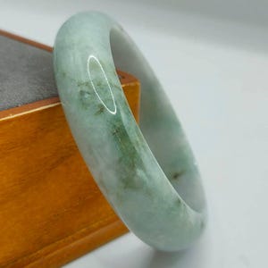 Peut inclure: Un bracelet en jade vert clair avec une finition polie. Le bracelet est fait de jade naturel et a une forme ronde et lisse.