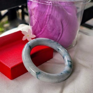 May include: A light green jade bangle bracelet with dark green veins. The bracelet is on a white surface.