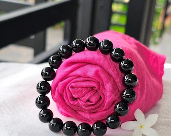 May include: A black beaded bracelet made of round, polished stones. The bracelet is wrapped around a pink fabric.