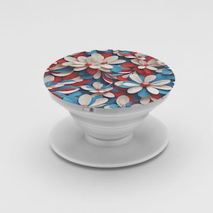 May include: White phone grip with a floral design in red, white, and blue. The pop-up grip features a round top with a pattern of stylized flowers and a white base for attaching to a phone or device.