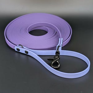 May include: A rolled-up, lavender-colored dog training leash with a light blue handle. The leash has a black metal clasp and rivets. The leash is designed for pet training and outdoor activities.
