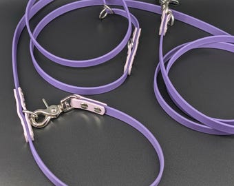 May include: A lavender-colored leash and collar set made of a smooth, flexible material. The set features silver-toned metal swivel snap hooks and D-rings, with light pink accents at the connection points secured by two small silver rivets.