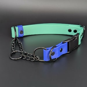 May include: A mint green collar featuring a blue accent strap, a black plastic side-release buckle, and black metal hardware including a chain link section with two circular rings. The collar is secured with black rivets and has a smooth, matte finish.