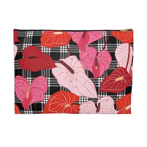 May include: A rectangular zippered pouch featuring a black and white plaid pattern. The pouch is adorned with a vibrant floral design of red, pink, and light pink anthurium flowers. The zipper is gold-colored.