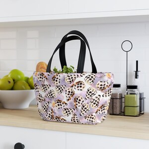 May include: A tote bag with a repeating pattern of black and white spotted shapes on a light purple background. The bag has black handles and is filled with bread and green herbs. The bag is sitting on a wooden countertop.