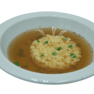 Peut inclure: Un bol blanc rempli d'un bouillon clair et d'un rond de nouilles jaunes garni d'oignons verts.