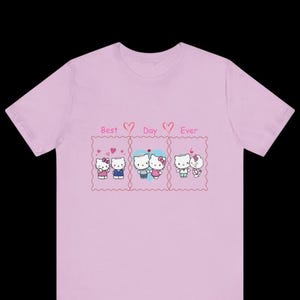 May include: A light pink t-shirt featuring three panels with cartoon characters and the text "Best Day Ever." Each panel depicts a couple with hearts. The shirt is a crew neck style.