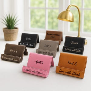 Peut inclure: Plusieurs supports de t&eacute;l&eacute;phone personnalis&eacute;s de couleurs vari&eacute;es, marron, noir, beige et rose. Chaque support affiche une police et un texte diff&eacute;rents, comme "Font 4" et "Brown with Gold". Les supports sont en mat&eacute;riau simili cuir.