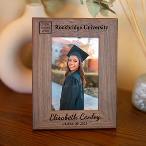 May include: A brown wooden picture frame with a graduation photo of a woman in a cap and gown. The frame has the text "Rockbridge University" and "Elisabeth Conley Class of 2025" engraved on it.
