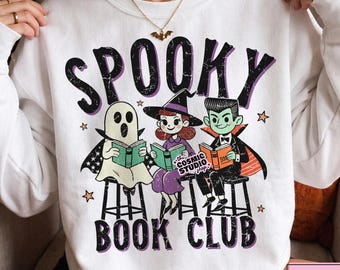 Pode incluir: Uma camisola branca de gola redonda com um gráfico de um fantasma, uma bruxa e um vampiro sentados em bancos a ler livros. O texto SPOOKY BOOK CLUB está escrito numa fonte preta desgastada. Pequenas estrelas cor de laranja estão espalhadas.