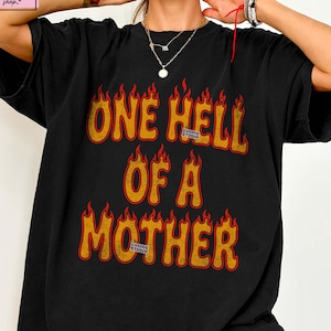 May include: Black t-shirt with the text "ONE HELL OF A MOTHER" in orange and yellow flames. The shirt has a distressed look and is a custom design.
