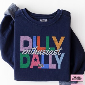May include: Navy blue sweatshirt with the words "DILLY enthusiast DALLY" in colorful, distressed lettering. The design includes a star and the text "the COSMIC STUDIO shop." Additional text indicates "PNG SOLID & DISTRESSED" and "DIGITAL DOWNLOAD."