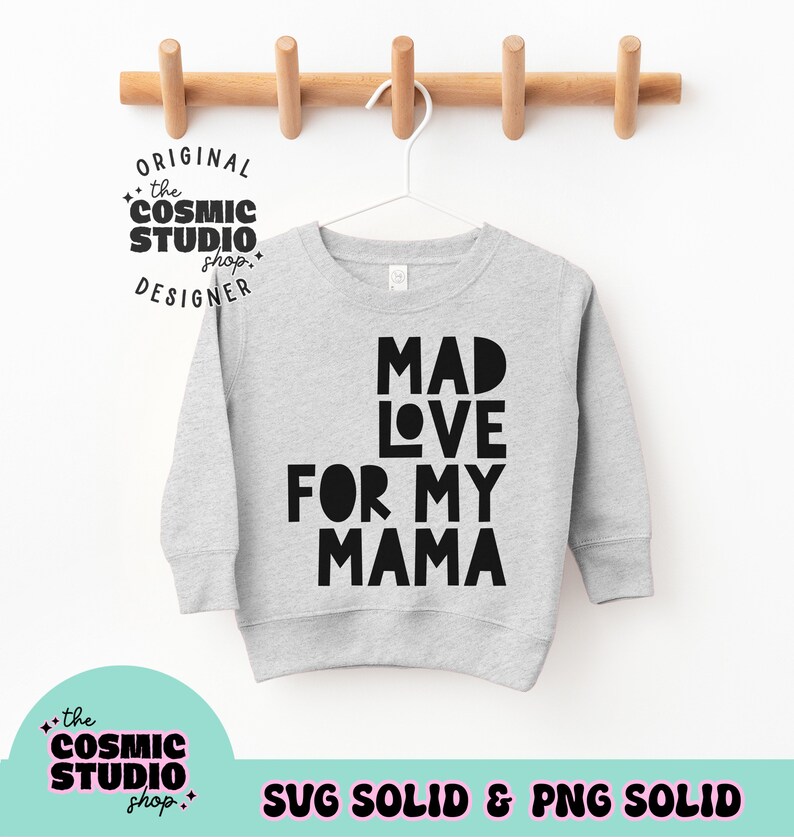 Puede incluir: Una sudadera gris claro con el texto "MAD LOVE FOR MY MAMA" en letras negras en negrita. La sudadera est&aacute; colgada de una percha blanca sobre un fondo blanco. La imagen tambi&eacute;n incluye el texto "the COSMIC STUDIO shop. DESIGNER" y "SVG SOLID & PNG SOLID".