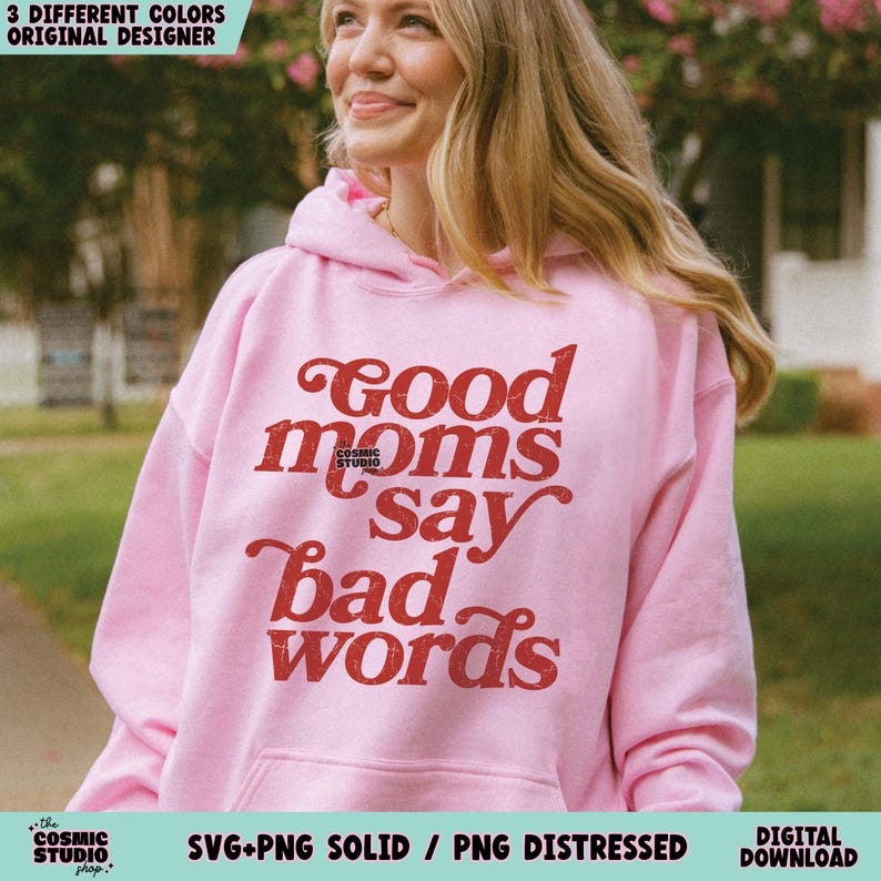 May include: A light pink hoodie with the text "Good moms say bad words" in red. The hoodie has a drawstring hood and a front pocket. The text is in a vintage, distressed style. The Cosmic Studio shop logo is at the bottom.