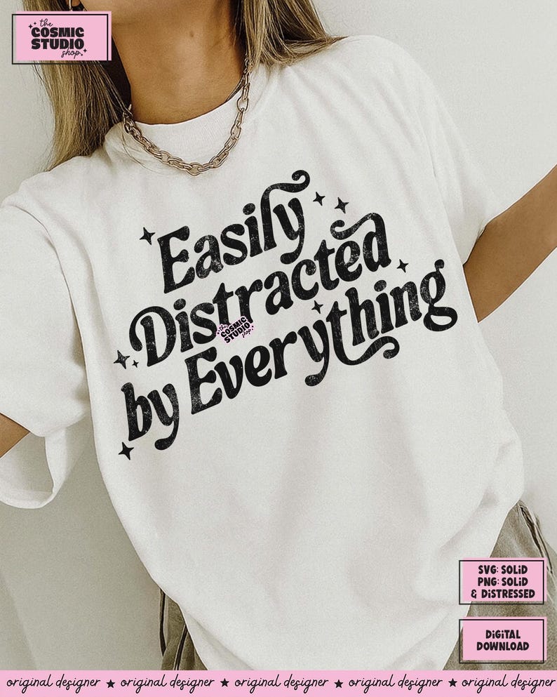 May include: A white t-shirt with the black text "Easily Distracted by Everything". The design includes star accents. The Cosmic Studio shop logo is visible. The shirt has a crew neck and short sleeves. A digital download is available.