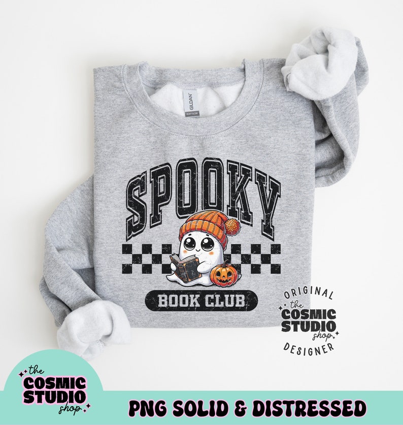 May include: A grey sweatshirt with a distressed graphic design featuring a ghost wearing a beanie and reading a book. The text "Spooky Book Club" is below the ghost. The text "Original the Cosmic Studio shop. Designer" is on the right side of the graphic.