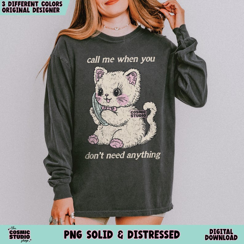 May include: Dark gray long-sleeve shirt featuring a vintage-style illustration of a kitten holding a telephone. The text reads "call me when you don't need anything." The shirt also has the text "Cosmic Studio" and "PNG Solid & Distressed".
