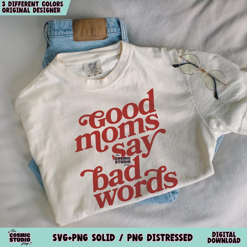 May include: Cream-colored t-shirt with the phrase "good moms say bad words" in red script. The shirt is folded over a pair of blue jeans, with a pair of round glasses resting on top. The image also includes text that says "3 different colors original designer".