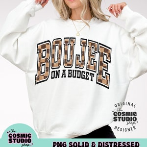 May include: White sweatshirt with a brown and black checkered graphic that says "Boujee on a Budget". The graphic has a distressed look. The sweatshirt is a mock-up and is not for sale.