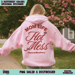 May include: A light pink hoodie with the words "MOM LIFE Hot Mess" in a distressed red font. The phrase "Chaos Is Mandatory" is below. The hoodie has a hood and long sleeves. The text "3 DIFFERENT COLORS ORIGINAL DESIGNER" is at the top.