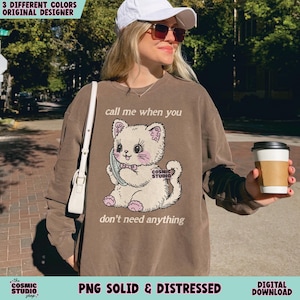 May include: Brown sweatshirt with a graphic of a cartoon cat holding a phone. The text on the sweatshirt reads "call me when you" above the cat and "don't need anything" below. The sweatshirt also has the text "Cosmic Studio" on the cat and at the bottom.