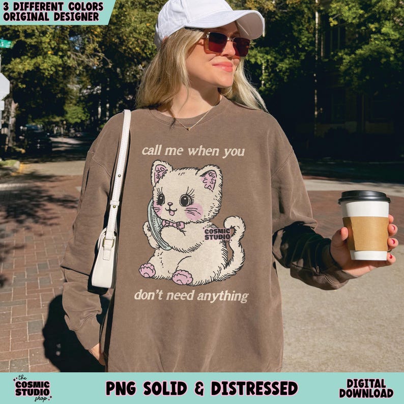 May include: Brown sweatshirt with a graphic of a cartoon cat holding a phone. The text on the sweatshirt reads "call me when you" above the cat and "don't need anything" below. The sweatshirt also has the text "Cosmic Studio" on the cat and at the bottom.