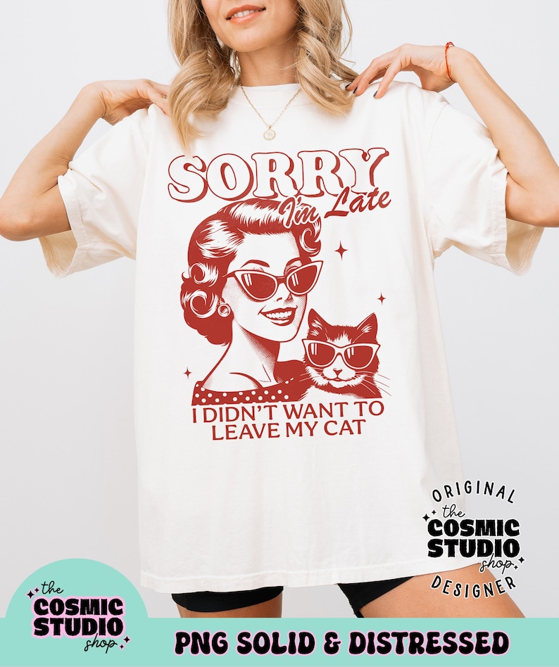 May include: Cream-colored t-shirt with a retro graphic of a woman and a cat, both wearing sunglasses. The text reads "SORRY I'm Late, I DIDN'T WANT TO LEAVE MY CAT." The shirt has a distressed design and is from The Cosmic Studio Shop.