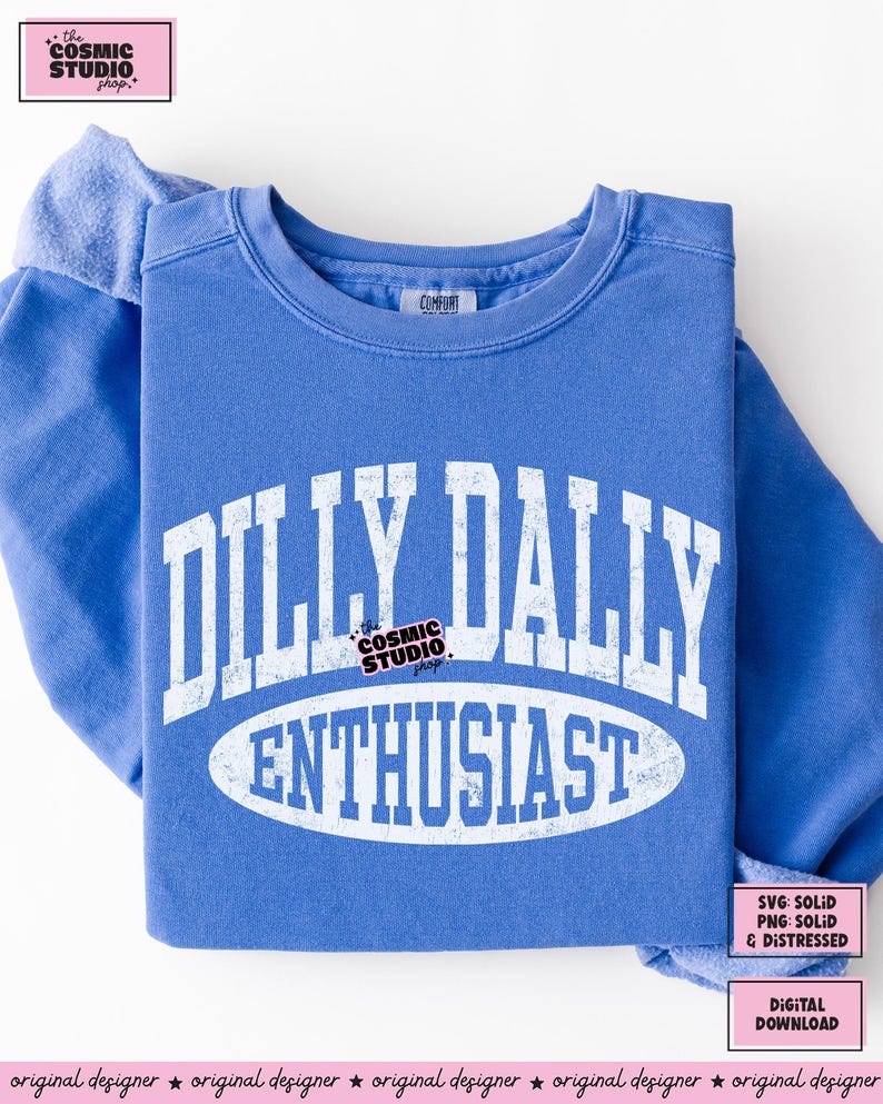 K&ouml;nnte beinhalten: Ein blaues Sweatshirt mit Rundhalsausschnitt und wei&szlig;em, abgenutztem Text, der DILLY DALLY ENTHUSIAST in einem College-Stil zeigt. Das Design enth&auml;lt eine ovale Form um das Wort ENTHUSIAST und ein kleines Logo f&uuml;r The Cosmic Studio Shop.
