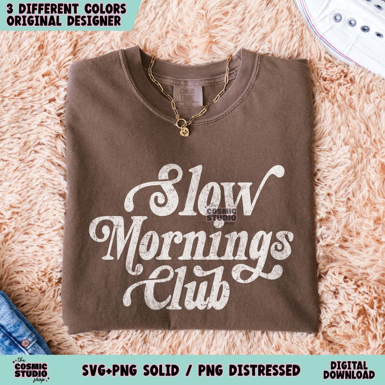 May include: A brown t-shirt with a white graphic that says "Slow Mornings Club" in a retro font. The graphic has a distressed look.
