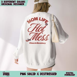 May include: White sweatshirt with the text "MOM LIFE Hot Mess Chaos Is Mandatory" in red. The sweatshirt also has the text "the COSMIC STUDIO shop." The image also includes the text "3 DIFFERENT COLORS ORIGINAL DESIGNER" and "PNG SOLID & DISTRESSED DIGITAL DOWNLOAD."