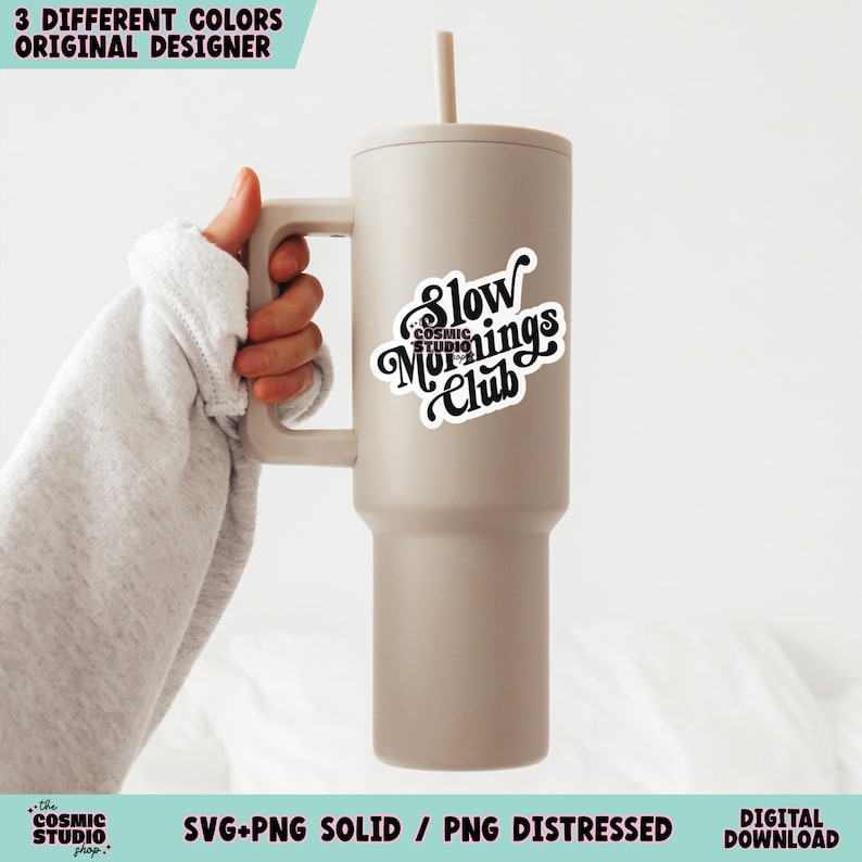 May include: A beige tumbler with a black and white sticker that says "Slow Mornings Club". The tumbler has a straw and a handle.