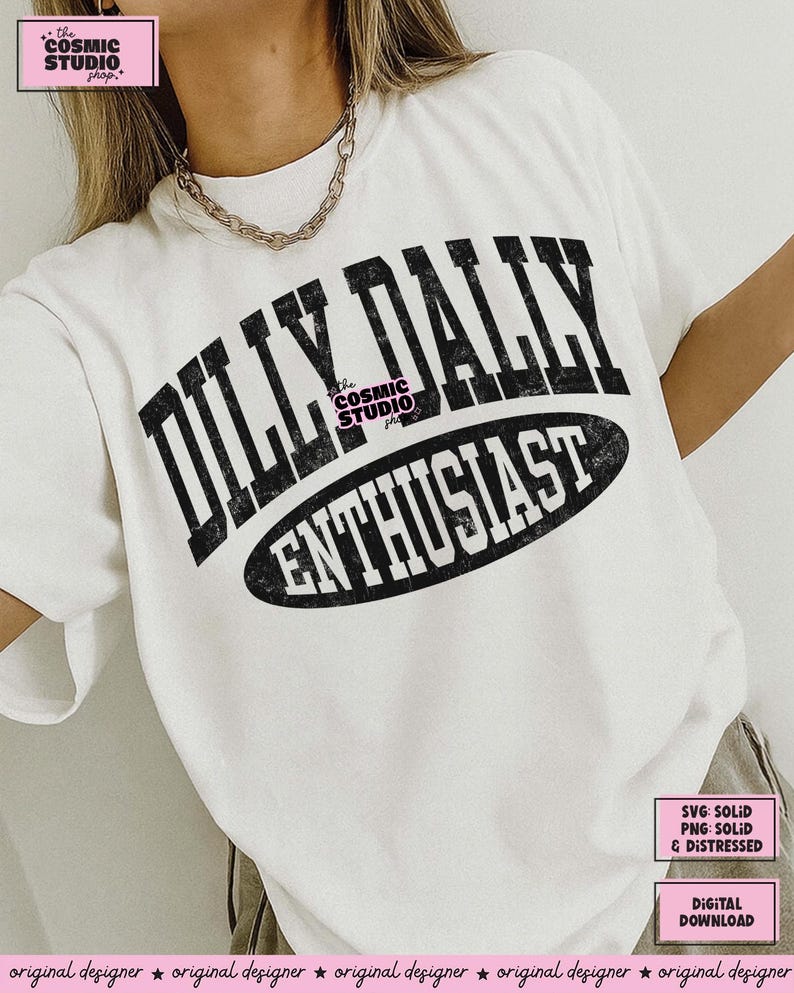 K&ouml;nnte beinhalten: Ein wei&szlig;es kurz&auml;rmeliges T-Shirt mit schwarzem, abgenutztem Text, der DILLY DALLY ENTHUSIAST lautet. Die Worte DILLY DALLY sind in einer gro&szlig;en, gebogenen Schriftart gehalten, w&auml;hrend ENTHUSIAST in einem schwarzen Oval steht. Das T-Shirt hat einen Rundhalsausschnitt.