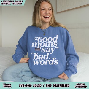 May include: A blue sweatshirt with the text "Good moms say bad words" in white. The sweatshirt has long sleeves and a crew neck. The words "Cosmic Studio" are also printed on the sweatshirt. The image also includes the text "3 DIFFERENT COLORS ORIGINAL DESIGNER".