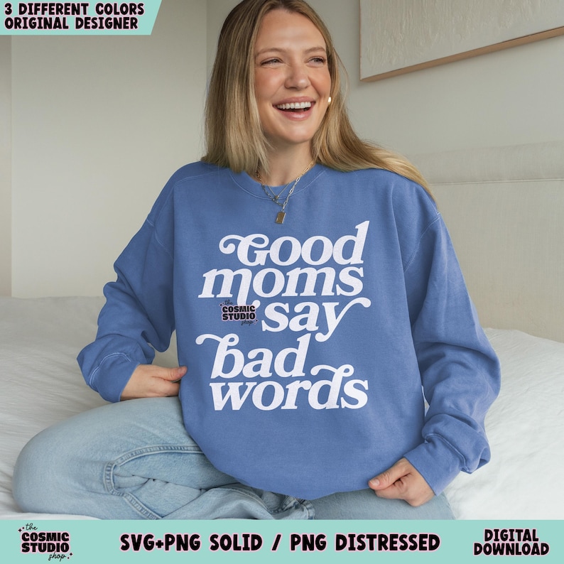 May include: A blue sweatshirt with the text "Good moms say bad words" in white. The sweatshirt has long sleeves and a crew neck. The words "Cosmic Studio" are also printed on the sweatshirt. The image also includes the text "3 DIFFERENT COLORS ORIGINAL DESIGNER".