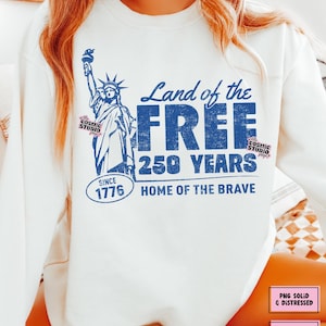 以下が含まれることがあります： 自由の女神と「Land of the Free, 250 Years, Since 1776, Home of the Brave」の文字が青色でプリントされた白いスウェットシャツ。「PNG Solid & Distressed」と「Digital Download」の文字も含まれています。