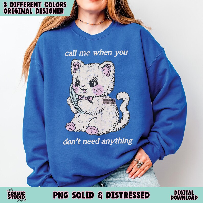 May include: Royal blue sweatshirt featuring a white cartoon cat holding a phone. The cat has pink cheeks and a pink bow. Text on the sweatshirt reads "call me when you don't need anything." The words "3 DIFFERENT COLORS ORIGINAL DESIGNER" are at the top.