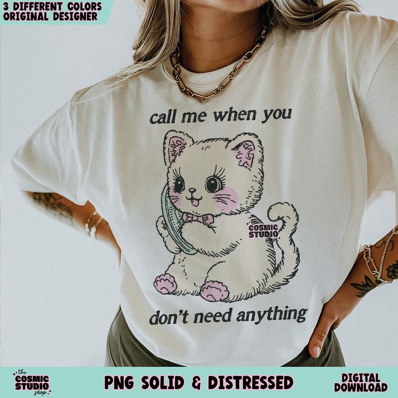 May include: Cream-colored t-shirt featuring a cartoon cat holding a phone, with the text "call me when you don't need anything." The cat has pink accents and is from the Cosmic Studio shop. The shirt is a digital download.