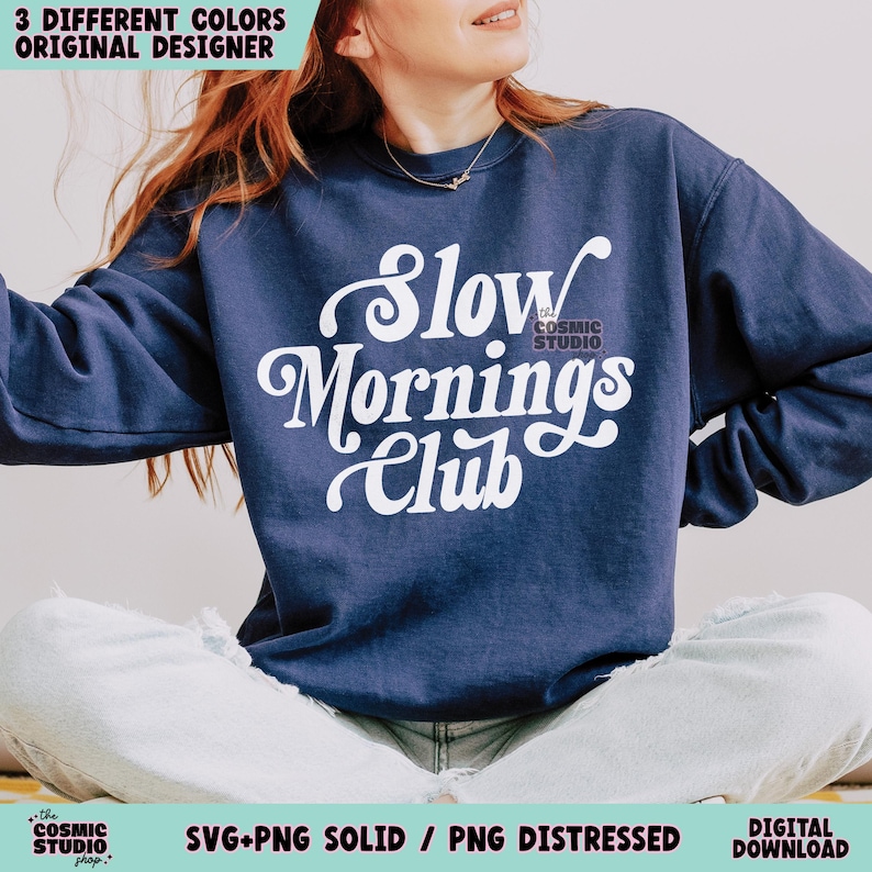 May include: A navy blue sweatshirt with the text "Slow Mornings Club" in white, retro-style lettering. The sweatshirt is being modeled by a person sitting with their legs crossed.