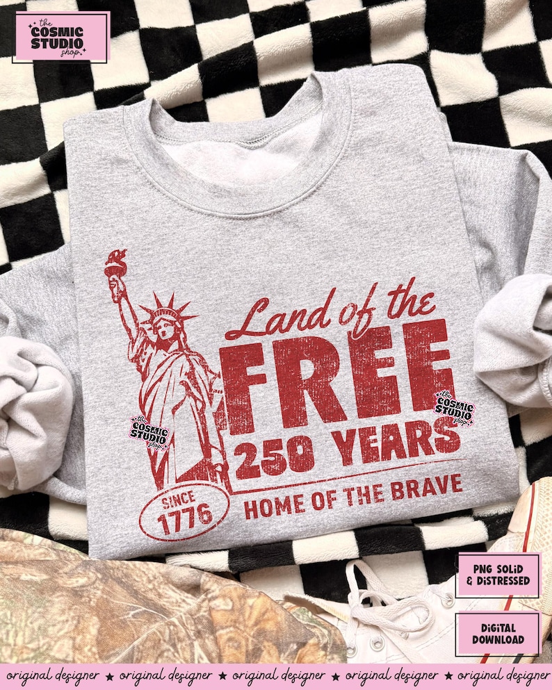 以下が含まれることがあります： 自由の女神と「Land of the FREE 250 YEARS HOME OF THE BRAVE SINCE 1776」の文字がプリントされた、グレーのスウェットシャツ。デザインには、Cosmic Studio shopのロゴも含まれています。