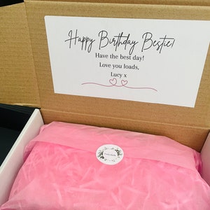 May include: A brown cardboard box with a white card inside that says "Happy Birthday Bestie! Have the best day! Love you loads, Lucy x". The box is open and filled with pink tissue paper.
