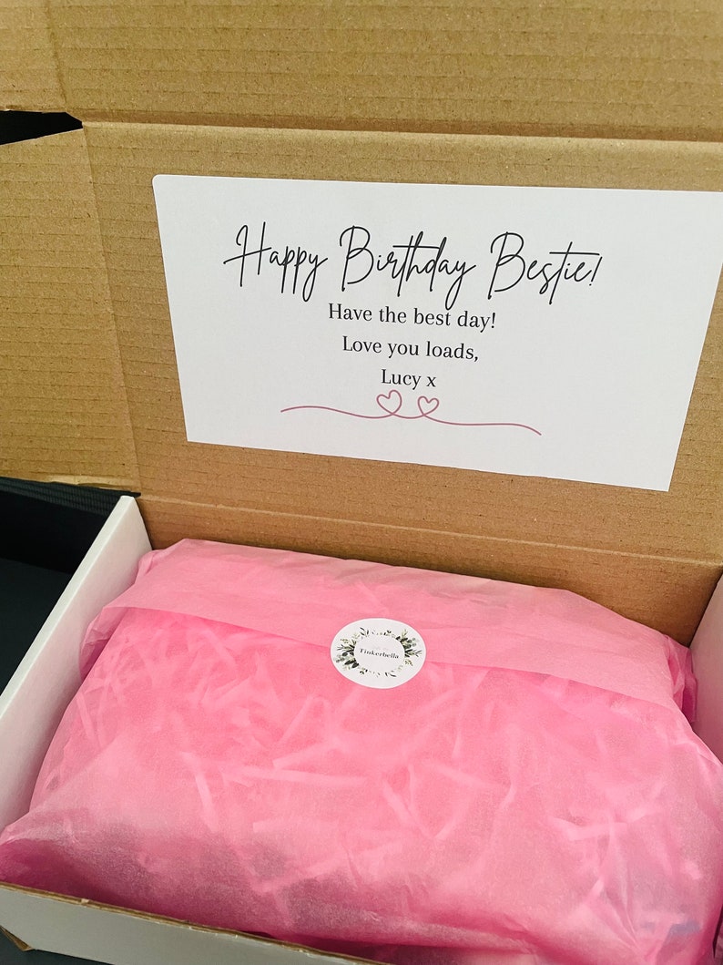 May include: A brown cardboard box with a white card inside that says "Happy Birthday Bestie! Have the best day! Love you loads, Lucy x". The box is open and filled with pink tissue paper.
