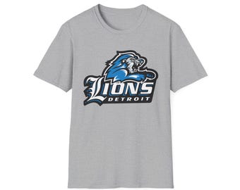 Könnte beinhalten: Ein graues T-Shirt mit dem Logo der Detroit Lions. Das Logo zeigt einen blauen Löwen mit dem Wort "Lions" in Weiß und Blau und "Detroit" in Weiß darunter. Das T-Shirt ist aus einem weichen Material.
