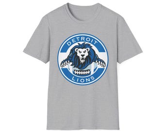 Könnte beinhalten: Ein graues T-Shirt mit dem Logo der Detroit Lions. Das Logo ist ein blau-weißes kreisförmiges Design mit den Wörtern "DETROIT" und "LIONS", die einen blauen Löwen mit weißem Gesicht und einem Football umgeben.