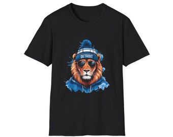 Könnte beinhalten: Schwarzes T-Shirt mit einem Löwen-Design. Der Löwe trägt eine Sonnenbrille, eine blaue Mütze mit der Aufschrift "DETROIT" und einen blauen Kapuzenpullover. Der Löwe hat eine braune Mähne und ist vor einem blauen Aquarellhintergrund platziert.