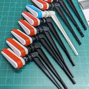 May include: A collection of 10 toilet flush handles with different colored tops. The handles are black and have a white and red or blue top. The handles are arranged in a row on a green cutting mat.