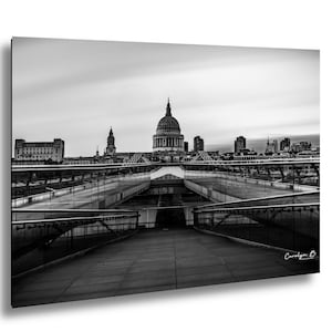 Può includere: Fotografia in bianco e nero di un paesaggio urbano con un ponte che conduce a un edificio a cupola. Il ponte ha ringhiere in vetro e una passerella in legno. Il cielo è nuvoloso. La foto è firmata "Carolyn B."