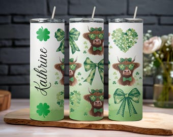 May include: Three stainless steel tumblers with a green, white, and black design featuring a Highland cow wearing sunglasses and a bow tie. The tumblers are decorated with shamrocks and bows. The name "Kathrine" is printed on one of the tumblers.