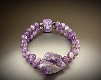 Op de afbeelding: Een dubbele amethyst armband met een grote amethyst kristallen hanger en een paarse kraal met een witte inscriptie.