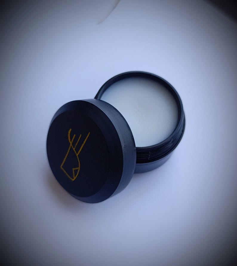 K&ouml;nnte beinhalten: Ein runder schwarzer Beh&auml;lter mit einem goldenen Logo eines stilisierten Fisches. Der Beh&auml;lter ist ge&ouml;ffnet und der Deckel liegt daneben. Der Beh&auml;lter ist mit einer wei&szlig;en Substanz gef&uuml;llt.