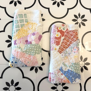 Puede incluir: Dos estuches rectangulares de tela acolchada con un diseño de patchwork de diversas telas de algodón con motivos florales, geométricos y lisos en tonos rosa, amarillo, azul, verde y blanco, con costuras a máquina visibles en las superficies.